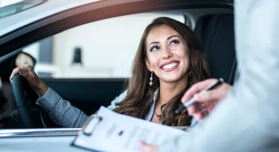 Chica sonriendo en su carro en casa comercial con ejecutivo